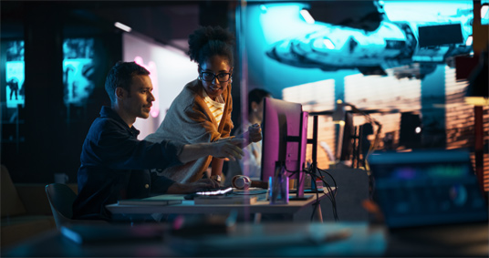 Dos personas trabajando frente a una computadora en un entorno futurista.